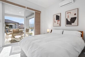 Habitación de hotel con una cama grande, una puerta corrediza de vidrio que da a un balcón y dos cuadros abstractos en la pared.