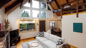 Ein gemütliches Wohnzimmer mit Kamin, großem Fenster, Essbereich und einem modernen Kunstwerk an der Wand.