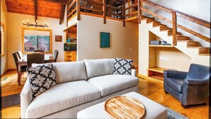 Ein geräumiges Wohnzimmer mit hoher Decke, einer Holztreppe und einem gemütlichen Sofa mit gemusterten Kissen.