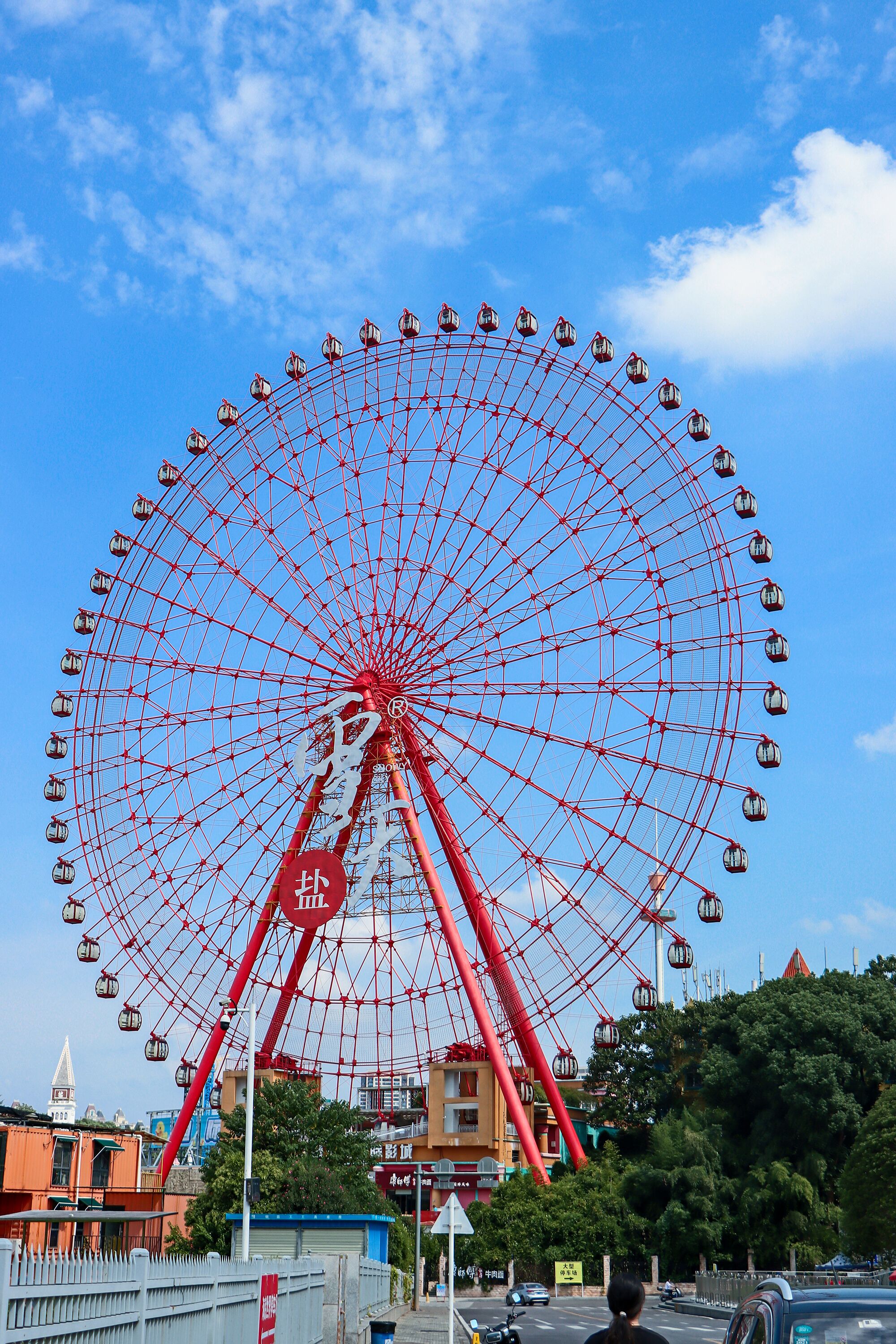 Une grande roue aux nacelles rouges, se détachant sur un ciel bleu clair.