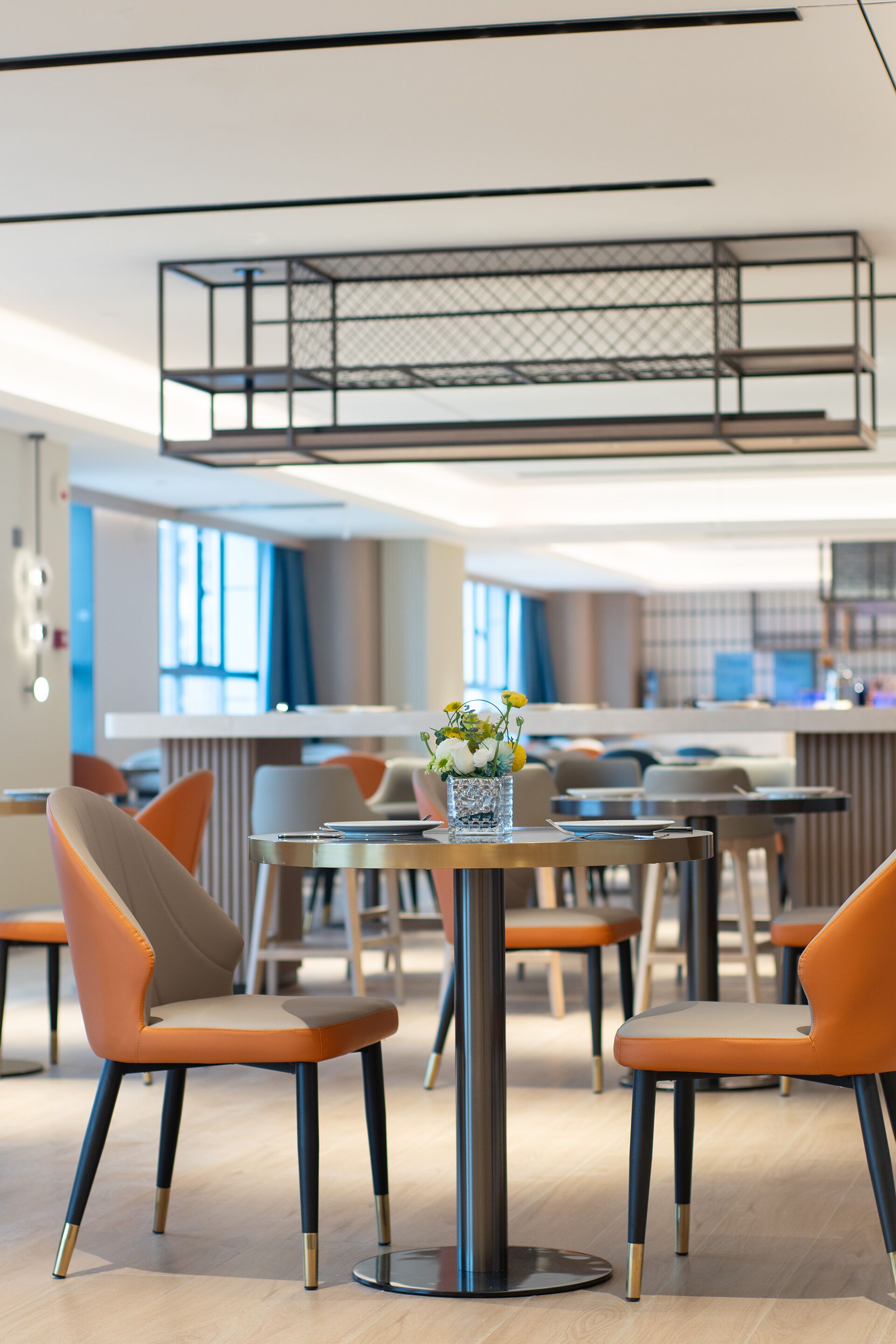 Ein moderner Essbereich mit orangefarbenen Stühlen, einem runden Tisch mit Blumenvase und einer Küche im Hintergrund.