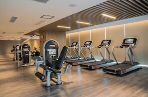 A gym with treadmills, weight machines, and a wooden floor.