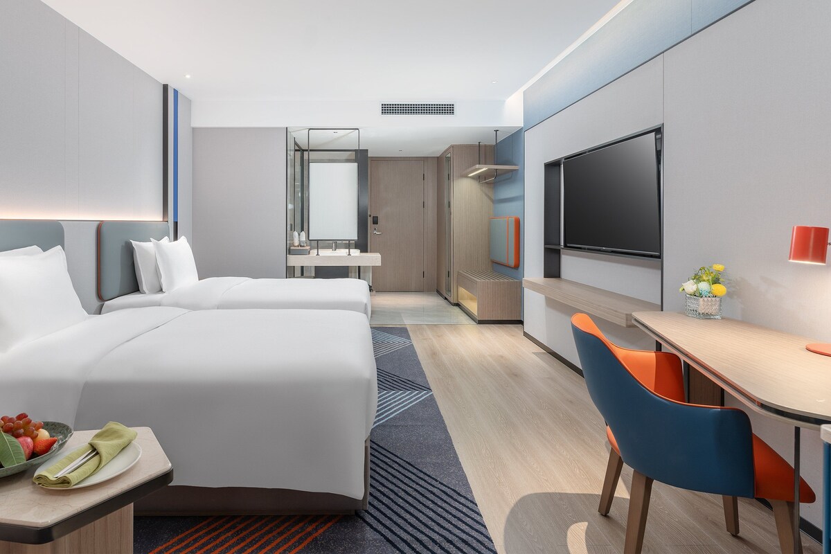 Ein modernes Hotelzimmer mit einem großen Bett, einem Schreibtisch, einem Fernseher und einer Sitzecke mit einem Sessel.