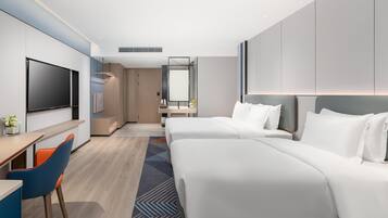 A modern hotel room with a large bed, a desk with a chair, a TV, and a bathroom with a mirror.
