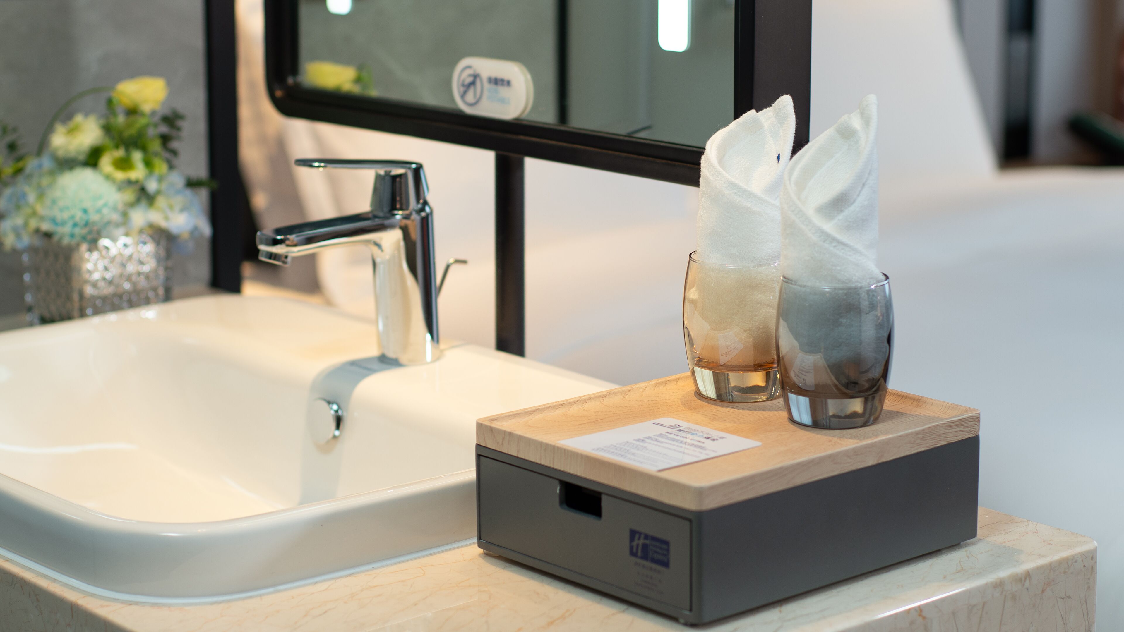 Ein Badezimmerwaschbecken mit einem modernen Wasserhahn, einer Taschentuchbox und zwei Gläsern auf einer Holztablett.