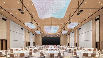A large conference room with round tables set for dining, equipped with projectors and a large screen at the front.