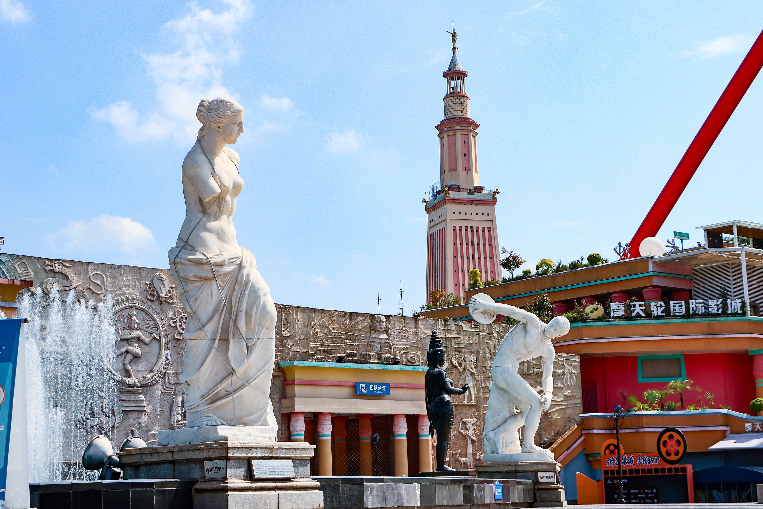 A statue of a woman, a fountain, and a building with a tower.
