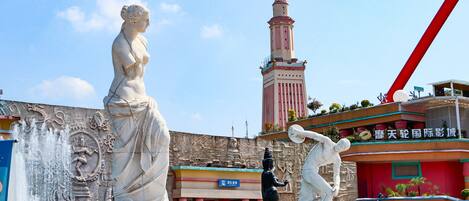A statue of a woman, a fountain, and a building with a tower.