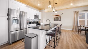 A modern kitchen with stainless steel appliances, a central island with bar stools, and a wooden ceiling.