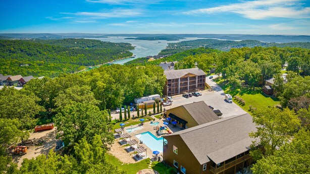A resort with a swimming pool, outdoor seating, and a view of a lake and forest.