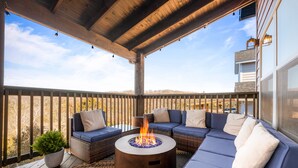 A covered outdoor seating area with a fire pit, wicker furniture, and a view of the landscape.