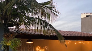 A pool area with a neon sign reading "Rogue House," wooden benches, and a palm tree. - RiqueHouse Hidro Piscina a 500m da praia (Marica)