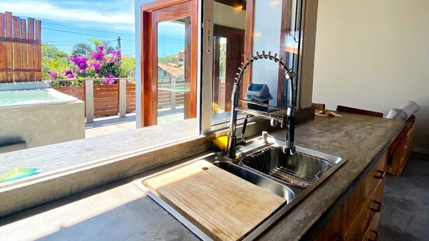 A kitchen with a large window, a wooden countertop, and a view of the ocean. - RiqueHouse Hidro Piscina a 500m da praia (Marica)