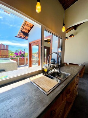A kitchen with a large window, a wooden countertop, and a view of the ocean. - RiqueHouse Hidro Piscina a 500m da praia (Marica)