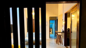 A hallway with a kitchen area visible through a glass door. There are wooden stools and a table in the kitchen. - RiqueHouse Hidro Piscina a 500m da praia (Marica)