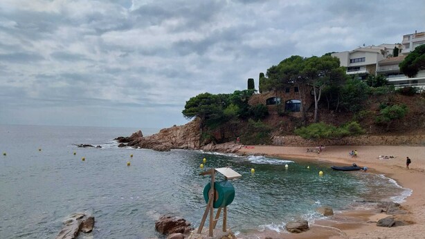 A rocky beach with clear water, a small boat, and buildings in the background. - Mar, Montaña y Relax con Vistas al mar (CT)