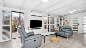 Un salon moderne avec un canapé en cuir gris, un fauteuil assorti, un téléviseur à écran plat et une bibliothèque.
