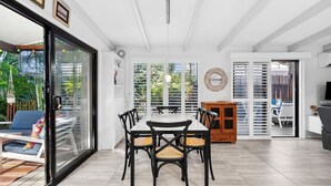 Un vaste espace de salle à manger comprenant une grande table et des chaises, un buffet en bois et une porte-fenêtre coulissante donnant sur un coin salon extérieur.