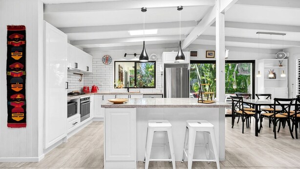Une cuisine moderne avec des meubles blancs, un îlot central doté de tabourets et un coin repas avec des chaises noires.