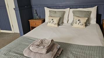 A neatly made bed with a folded towel, two patterned pillows, and a bedside table with a glass container.