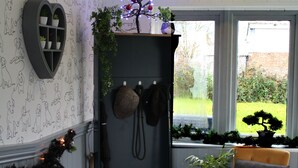 A corner room with a dark blue cabinet, a small chair, a heart-shaped decoration, and a window with a view of greenery. - Dog and Partridge Inn (Calne)