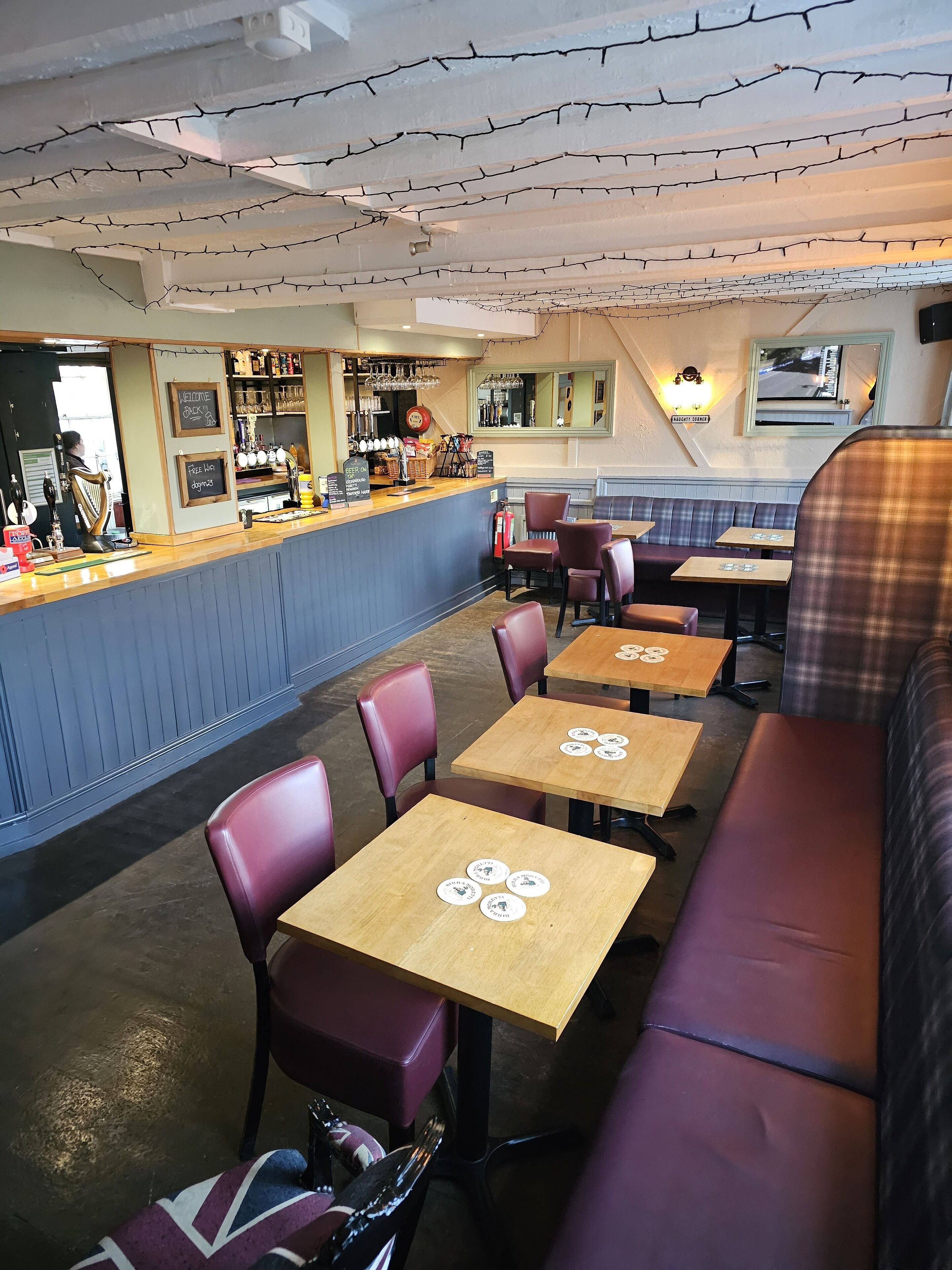 A restaurant interior with wooden tables and cushioned booths, a bar area with a counter, and a seating arrangement that includes a mix of booths and tables.