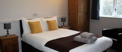 A neatly made bed with white and brown bedding, a wooden wardrobe, and a window with curtains.