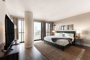 A modern hotel room with a large bed, a flat-screen TV, a desk, and a view of the city.
