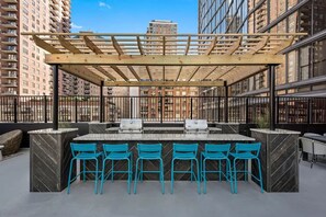 An outdoor bar area with a wooden pergola, a marble counter, and blue chairs.