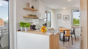 A modern kitchen with white cabinetry, a wooden countertop, and a dining area with a table and chairs. - Bunk 21 Heiligenhafen Studio-Apartment (Heiligenhafen)