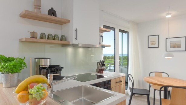 A modern kitchen with a glass backsplash, stainless steel appliances, and a dining area with a wooden table and chairs. - Bunk 21 Heiligenhafen Studio-Apartment (Heiligenhafen)