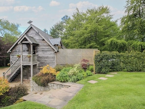 A wooden cabin with a porch, stone steps, and a garden with various plants.