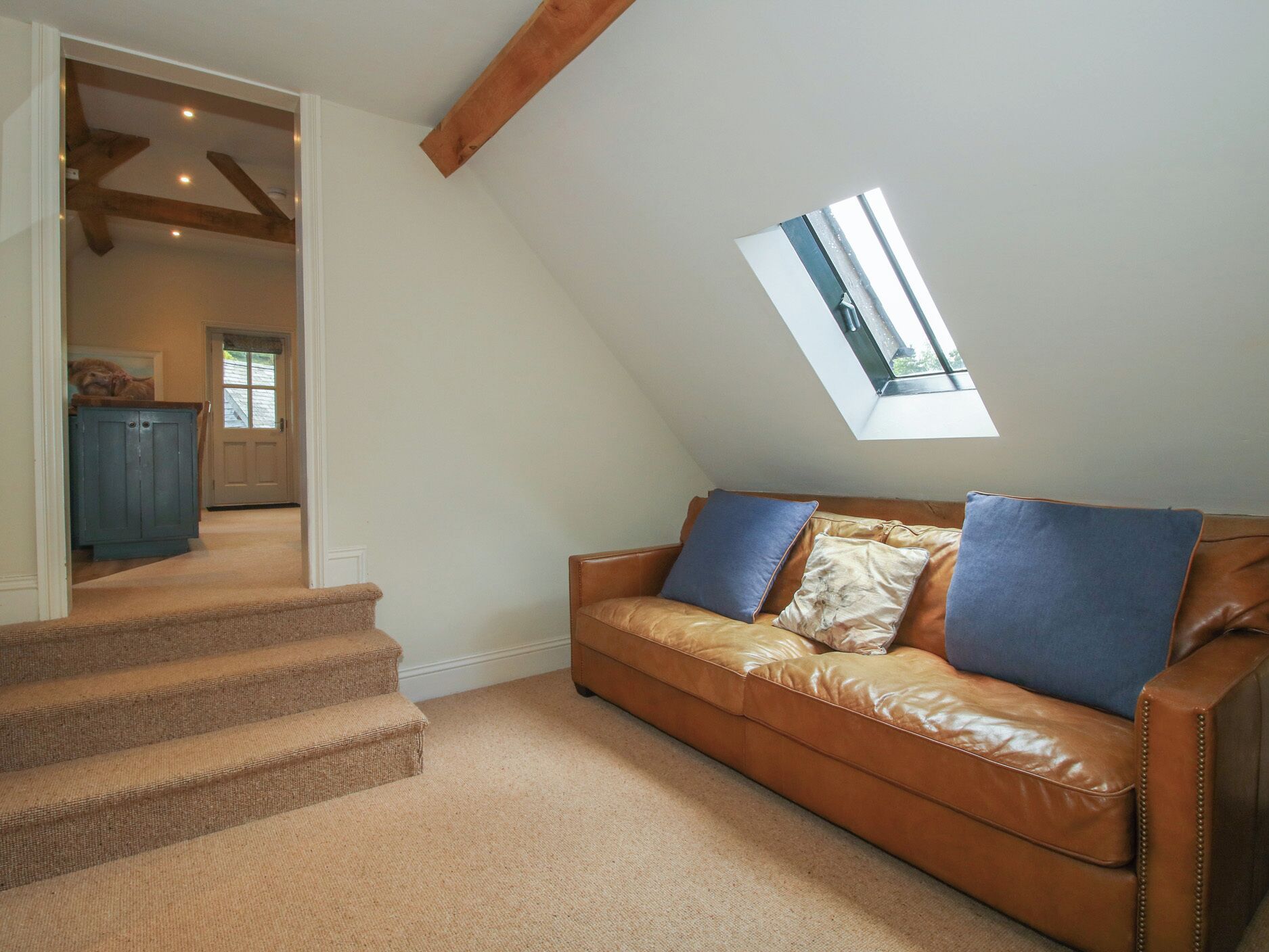 A loft bedroom with a sloped ceiling, a brown leather sofa with blue cushions, and a skylight.