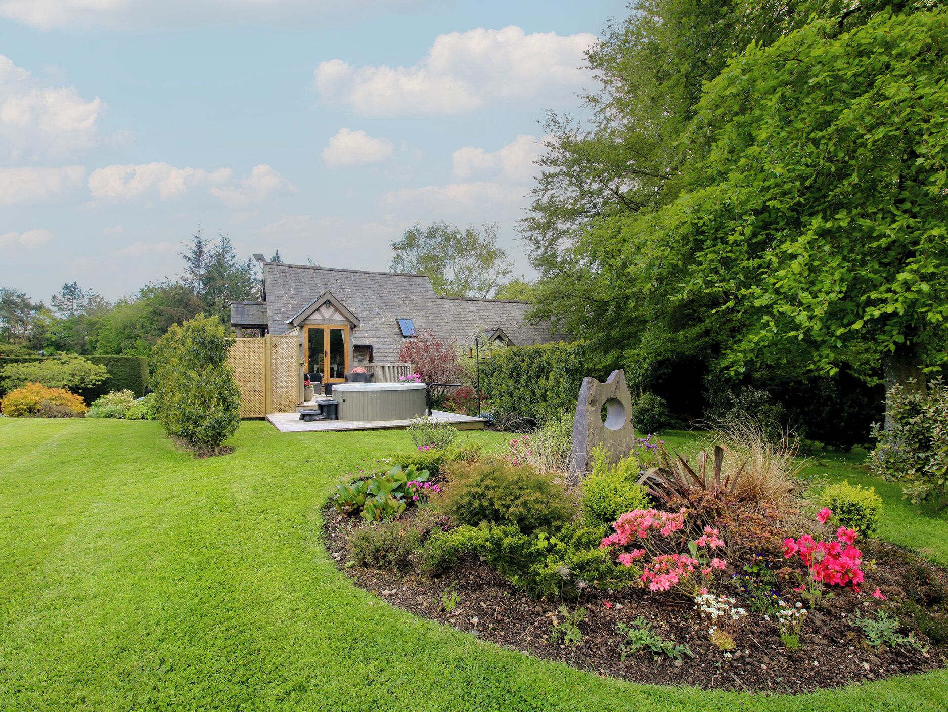 A house with a garden, a hot tub, and a wooden deck.