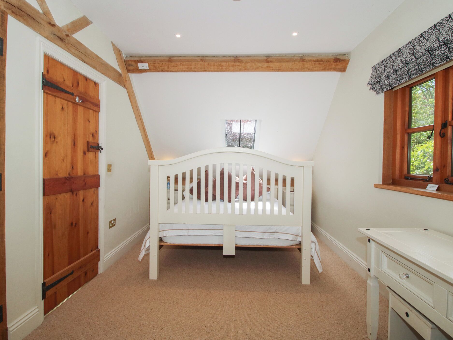 A room with a white crib, wooden beams, a window, and a white dresser.