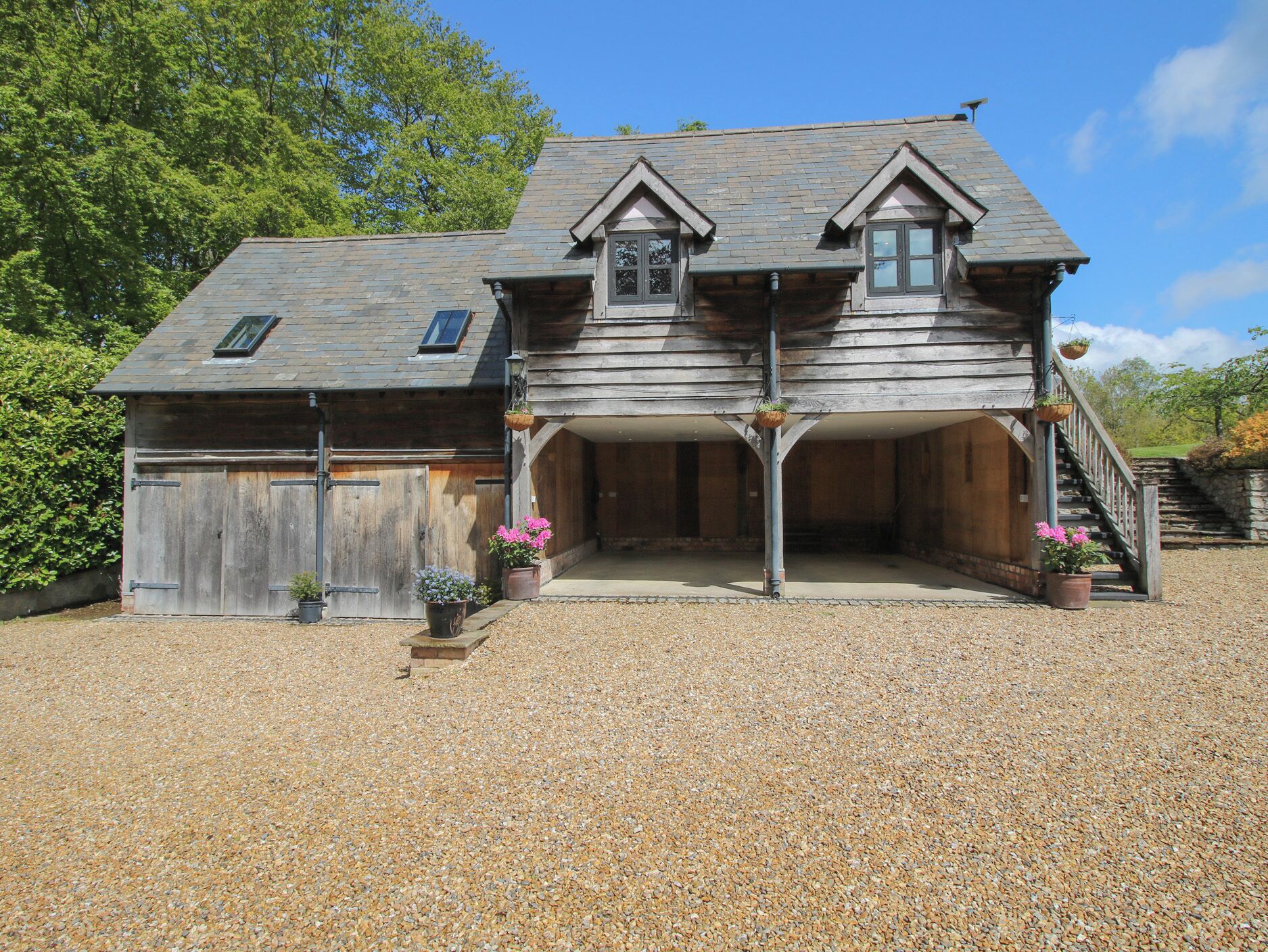 A wooden house with a gravel driveway, a covered porch, and a staircase leading to the entrance.