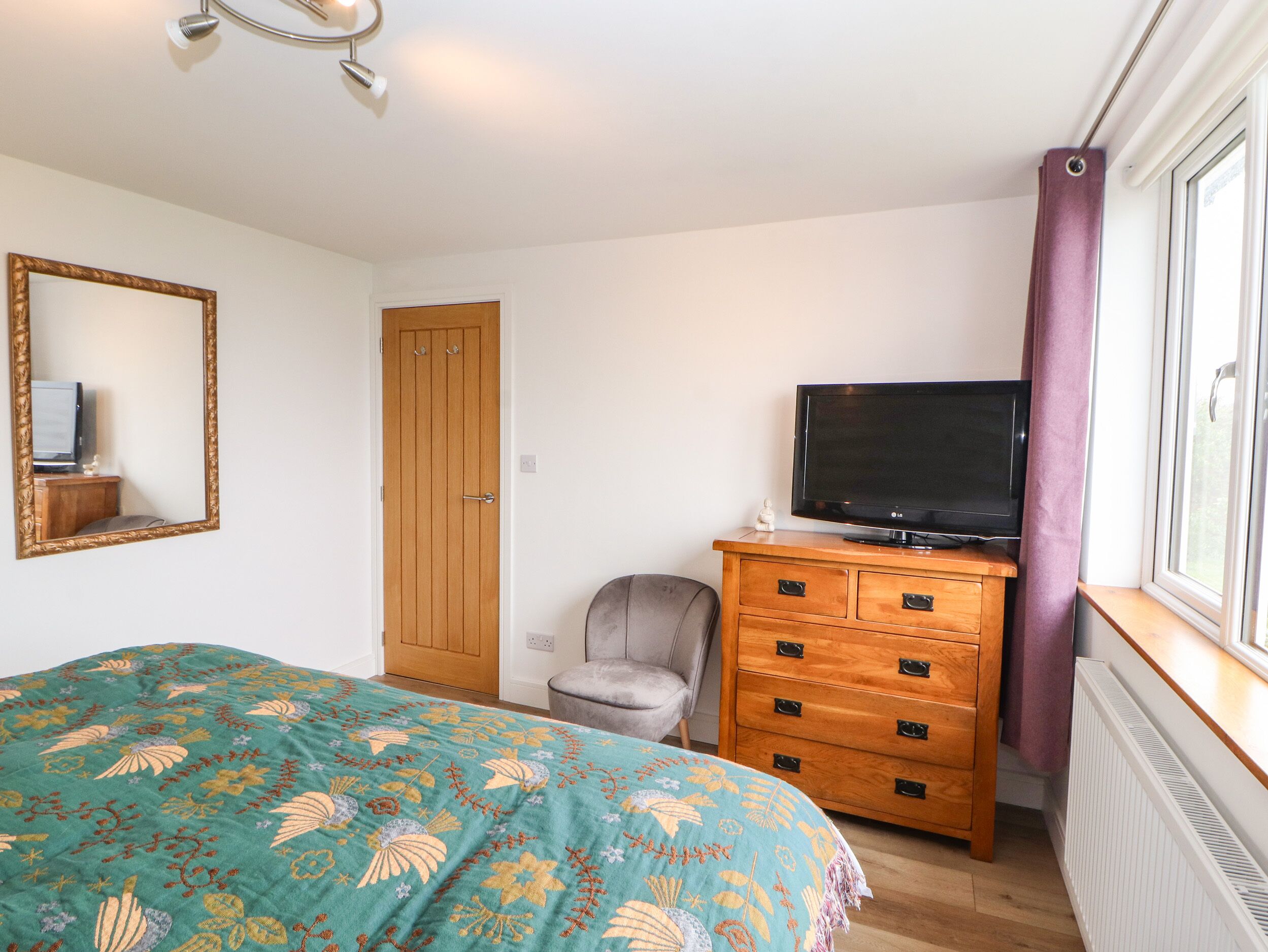 Een slaapkamer met een bed, een dressoir, een televisie, een stoel en een deur.