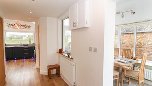 Una cocina moderna con suelo de madera, un pequeño comedor con mesa y sillas, y vistas a una pared de piedra a través de una ventana.