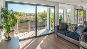 A modern living room with a large sliding glass door leading to a balcony, a sofa with patterned cushions, and a potted plant. - Step into indulgence, where every detail is tailored for your comfort. (Cradley, near Malvern)