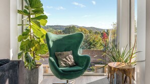 A green armchair with a cushion, a wooden side table, and a large window with a view of hills and trees. - Step into indulgence, where every detail is tailored for your comfort. (Cradley, near Malvern)