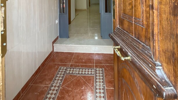 A hallway with a wooden door, a tiled floor, and a ceiling light.