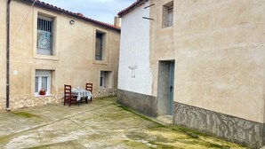 A courtyard with a table and chairs, a stone wall, and a building with a tiled roof.
