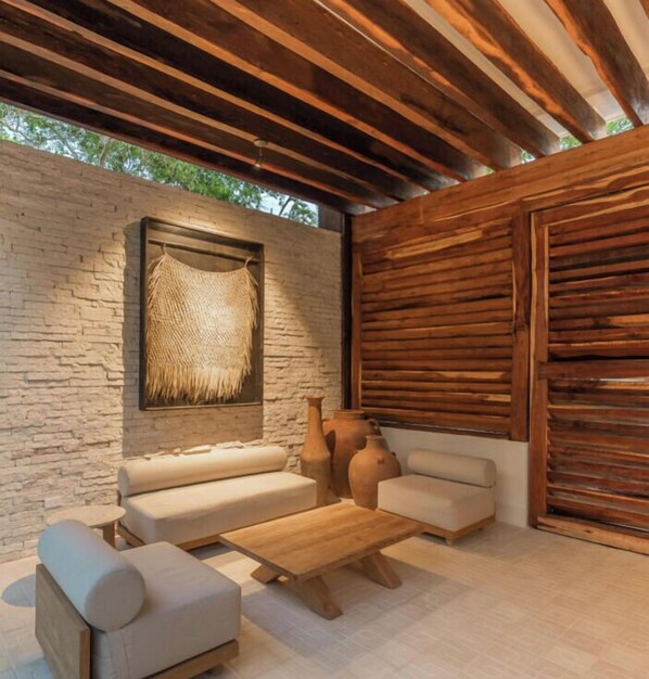 Een terras met een stenen muur, houten plafond en een wandkleed van geweven materiaal.