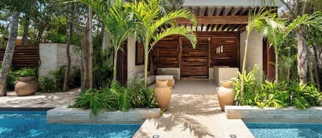 A pool area with a wooden pergola, palm trees, and a clear sky.