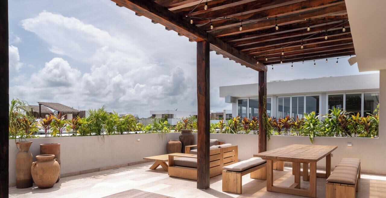 Eine Terrassengruppe im Freien mit Holzmöbeln, einer Pergola und Kübelpflanzen.