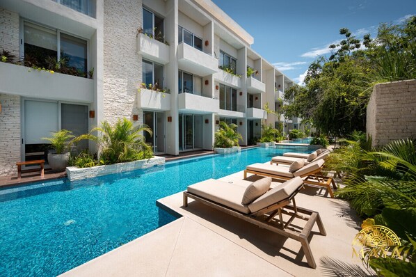 A modern hotel with a swimming pool, lounge chairs, and lush greenery.