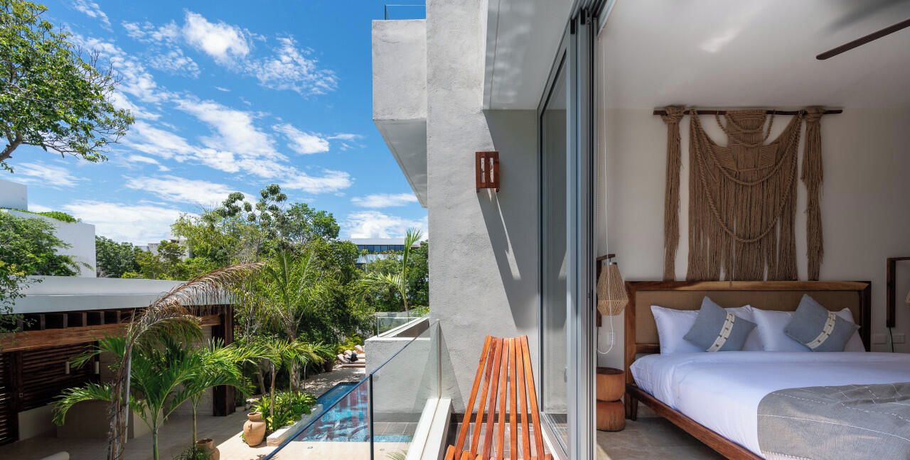 Habitación de hotel moderna con una cama grande, una silla de madera, una piscina pequeña y vistas a la vegetación circundante.