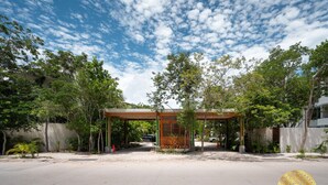 A building with a covered entrance, surrounded by trees and a clear sky. - NHOA 207C Lux 1BR Condo Pool View in Aldea Zama (Tulum)