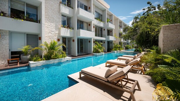 A modern hotel with a swimming pool, lounge chairs, and lush greenery.