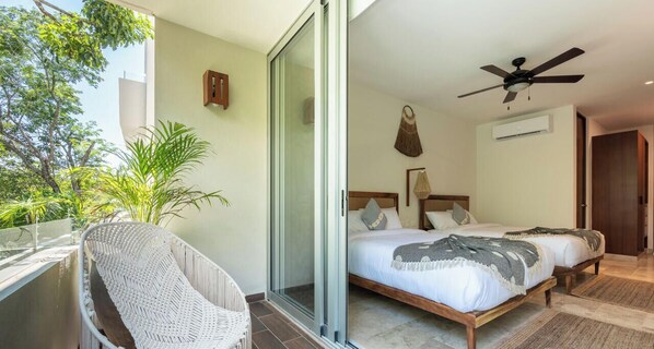 Een slaapkamer met een bed, een plafondventilator en een balkon met een rieten stoel.